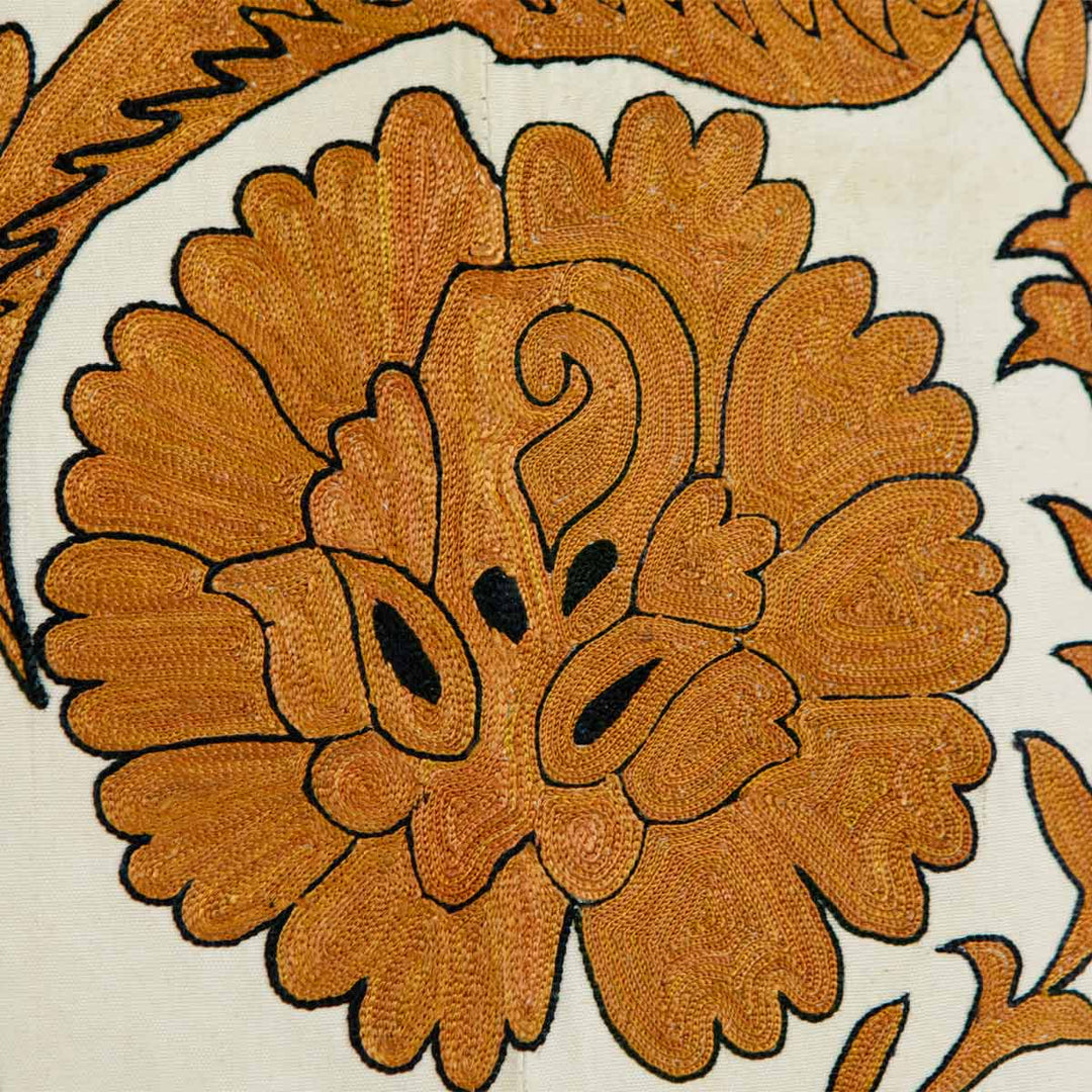 Close up view of Mekhann's caramel botanical throw, showing up close one of the floral hand embroidered design motifs, in a wonderful warm caramel tone.