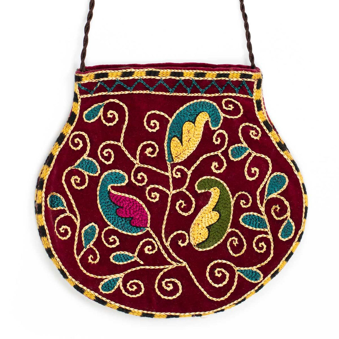 Front view of Mekhann's botanical deep maroon velvet pouch, adorned by embroidered botanical patterns in blue, green, and yellow.