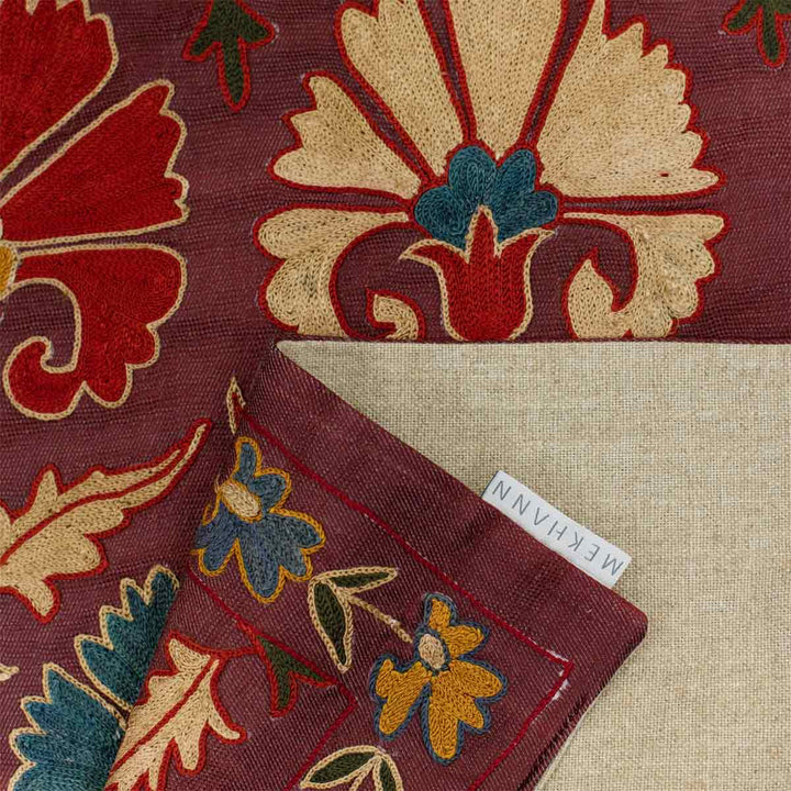 Folded view of Mekhann's purple carnations petite throw, showcasing the lining of the back of the runner with the Mekhann label.