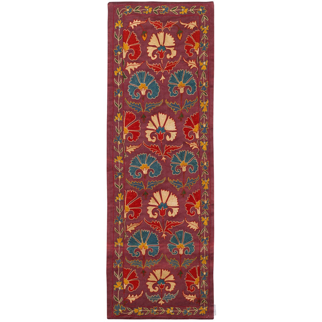 Front view of Mekhann's purple carnations petite throw, adorned with a lush carnation pattern in shades of gold, blue, and green, that have all been hand embroidered on a purple silk base.