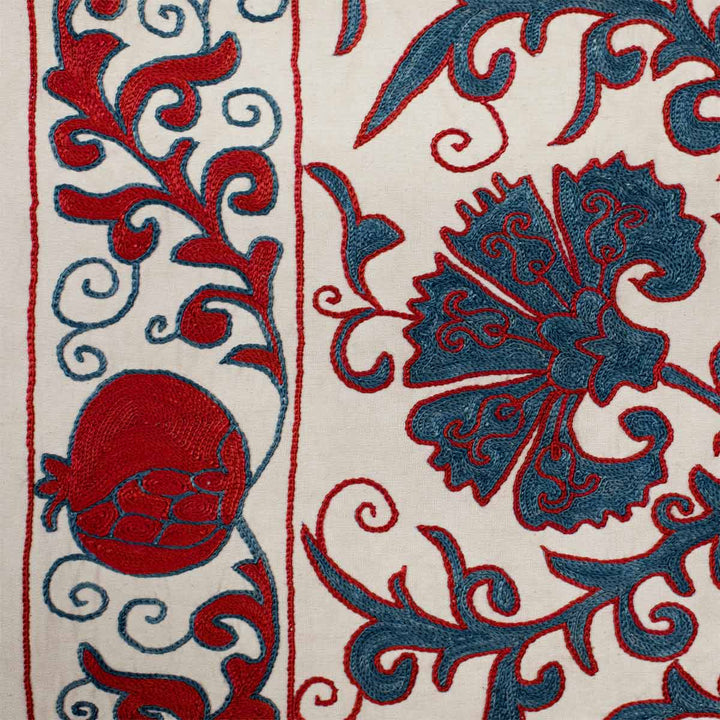 Detail view of Mekhann's cream carnations tree throw, showing a bright red pomegranate motif embroidered into the boarders of the throw.