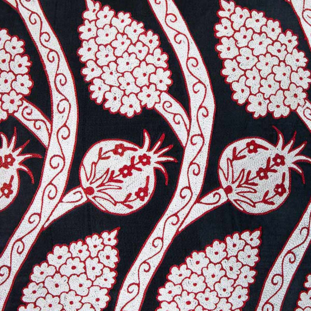 Close up view of Mekhann's black grapes and pomegranates embroidered cushion, revealing the detail and texture of the pomegranate and grapes design motifs, showing how they have been embroidered onto black silk.