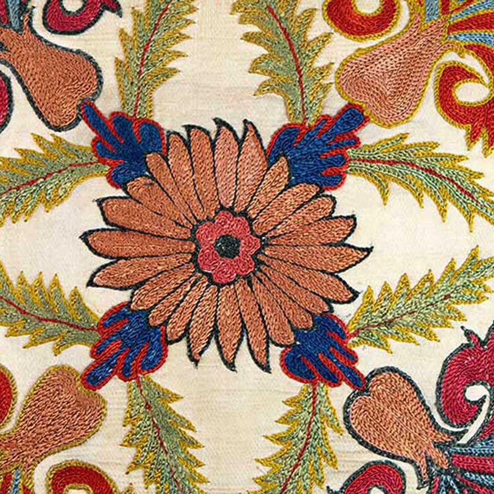 Close up view of Mekhann's cream carnations embroidered cushion, where we can see the centre point of the cushion that is a hand embroidered flower motifs in the colours orange, blue, and red. 