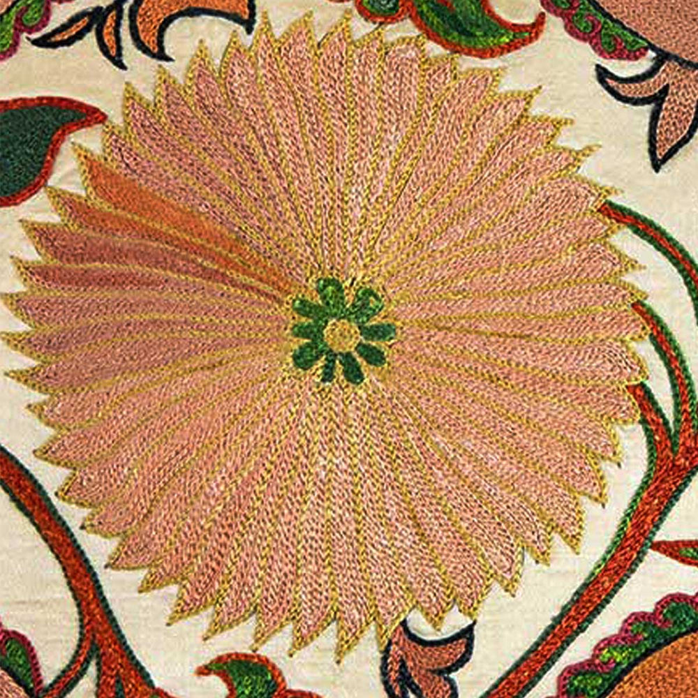 Close up view of Mekhann's hand embroidered silk iznik cushion in cream. On display is a light orange hand embroidered flower motif that has been embroidered onto a base of cream coloured silk.