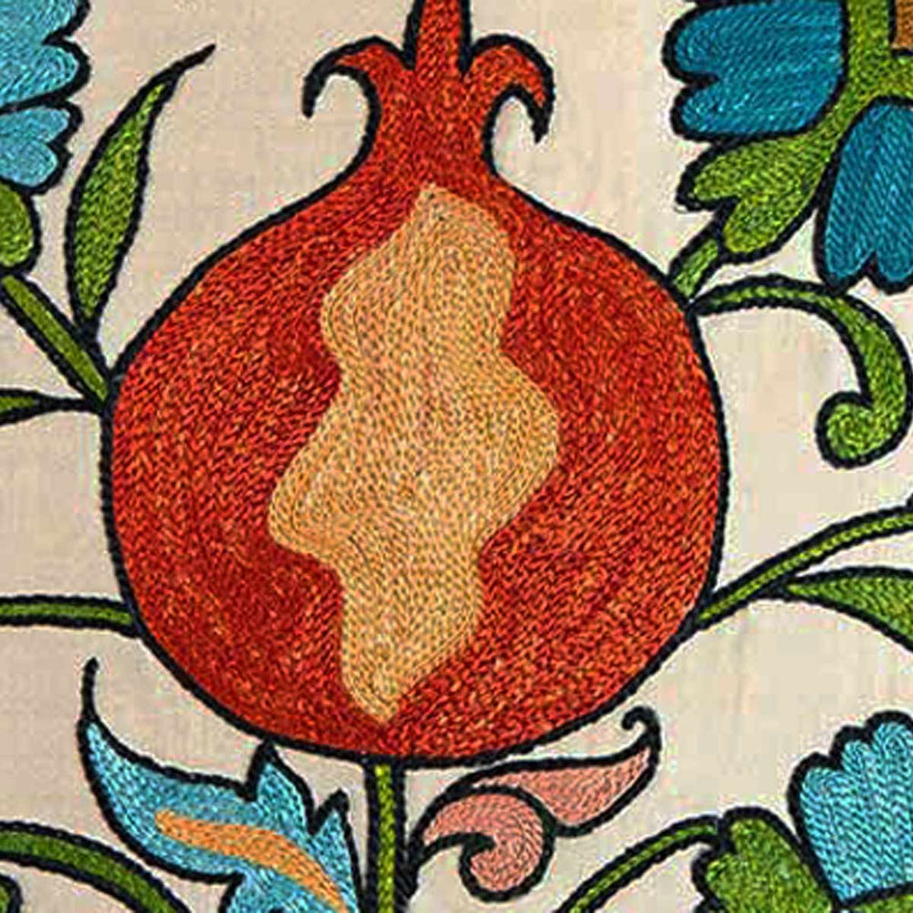 Close up view of Mekhann's cream tulips and pomegranates embroidered cushion,  focusing on the main red and orange pomegranate motif that has been outlined using black silk yarns, all on a base of cream coloured silk.