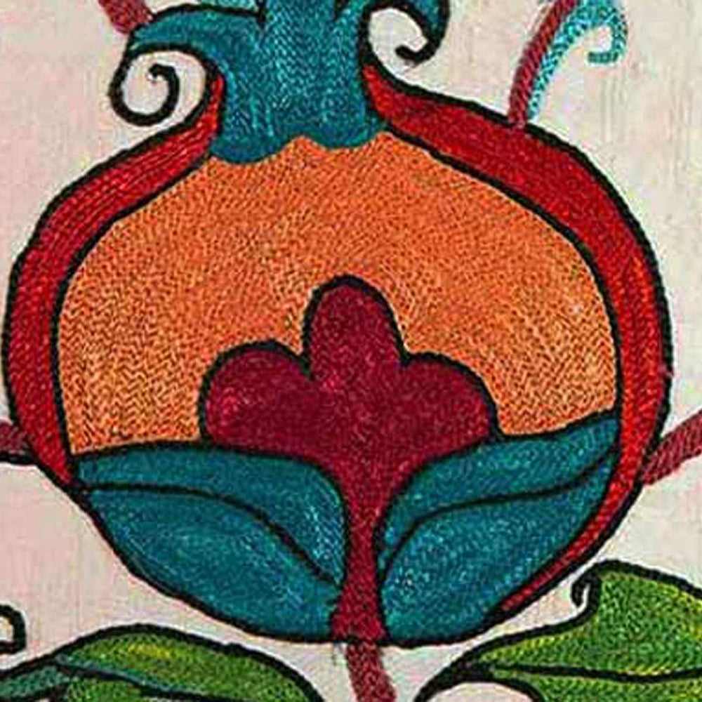 Detailed view of Mekhann's cream Tulips and Pomegranates embroidered cushion, showing one of the hand embroidered pomegranate motifs up close in the colours blue, red and orange on a cream coloured silk base.