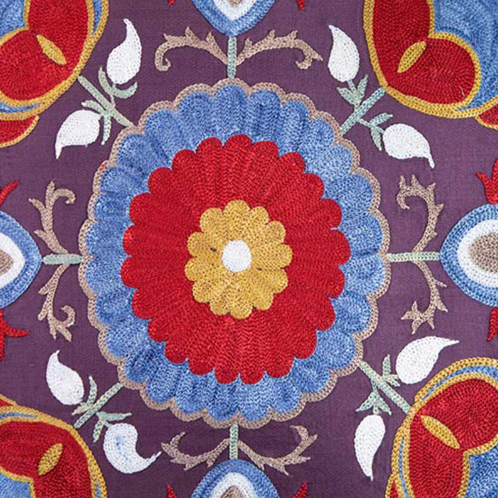 Close up view of Mekhann's multicoloured lotus embroidered cushion, focusing the central flower motif of the cushion that has been created using blue, red and yellow silk yarns.