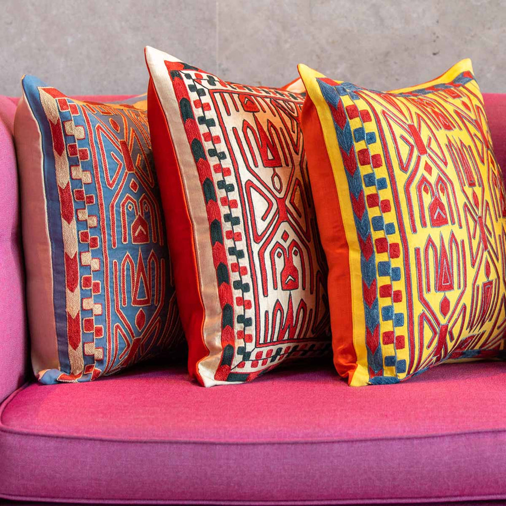 Mekhann's colourful Elibelinde embroidered silk cushions arranged on a vibrant pink sofa, showcasing detailed stitching and double-sided finishes