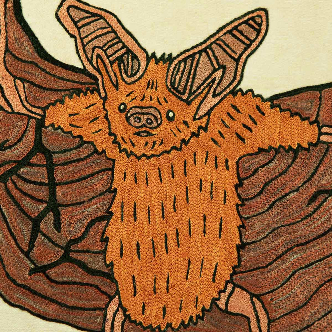 Close up of Mekhann's cream silk hand embroidered bat artwork, giving a more detailed look at the face of the bat, all of the details of the body have been outline in black to give more definition to the features of the hand embroidered bat.