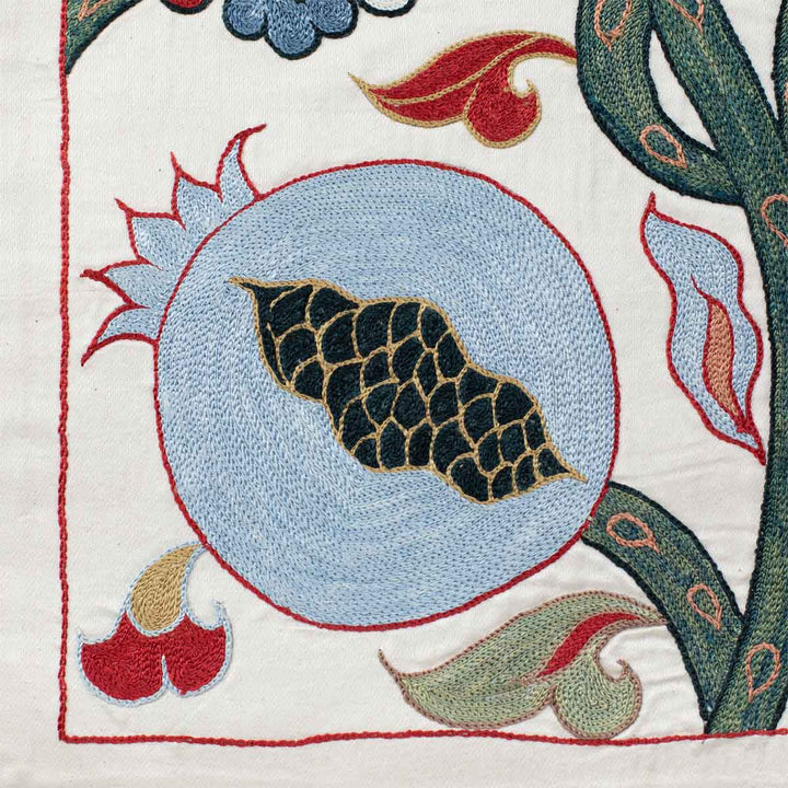 Close up view of Mekhann's cream ottoman vines runner, displaying one of the pomegranate embroidered motifs in light blue, greens and reds on cream coloured silk.