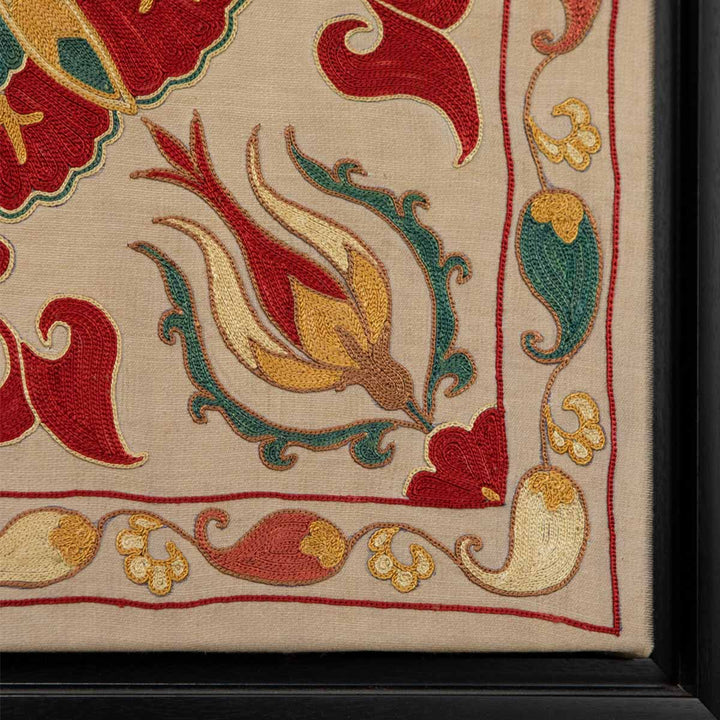 Corner view of Mekhann's cream silk botanicals artwork, showing the edge of the black frame, also displaying the corner boarder embroidered onto the cream silk.