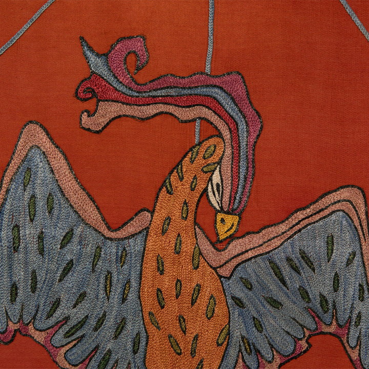 Close up view of Mekhann's maroon silk hand embroidered phoenix artwork, revealing the detail of the phoenix head, embroidered using pink, blue, red, and yellow silk yarns.