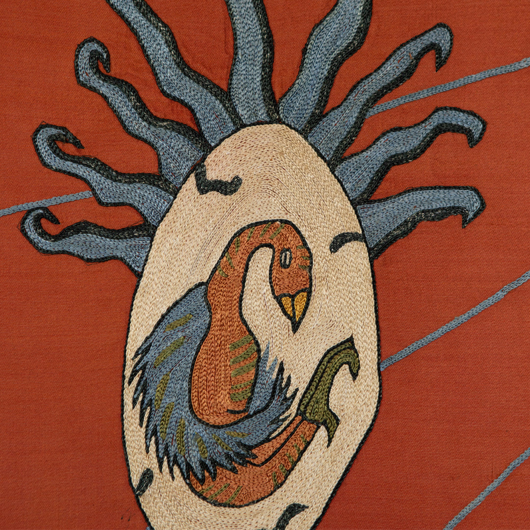 detail view of Mekhann's maroon silk hand embroidered phoenix artwork, displaying the phoenix egg that has been mainly embroidered in cream and blue silk against the maroon base.
