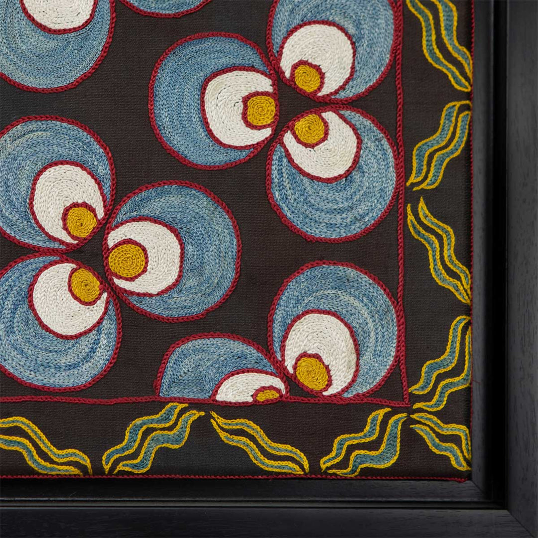 Corner view of Mekhann's black silk cintamani artwork, showing the black corner of the frame. We can also see the blue and yellow patterns that cover the edge of the textiles.