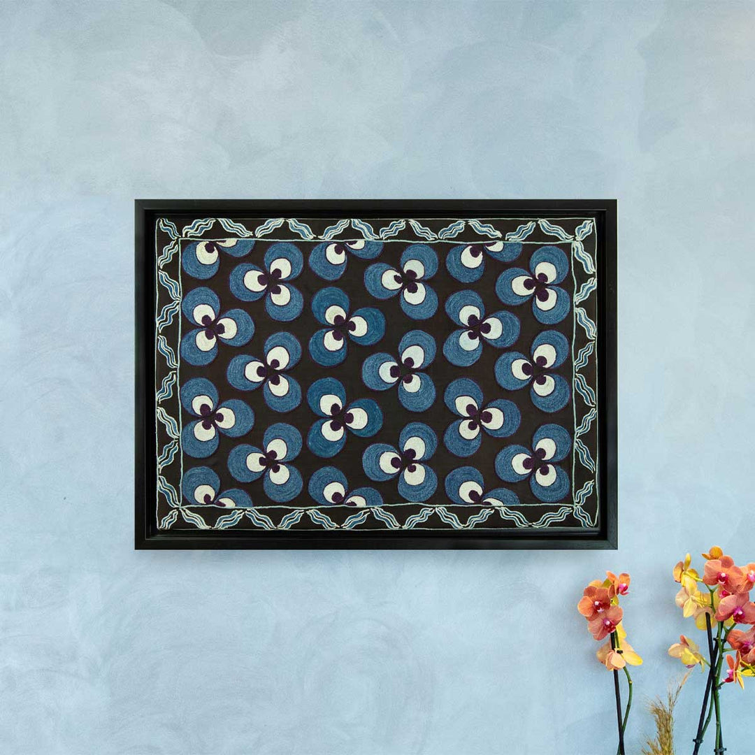 In use view of Mekhann's hand embroidered black silk cintamani artwork, showing how the black and blue framed artwork would look hung on a wall.