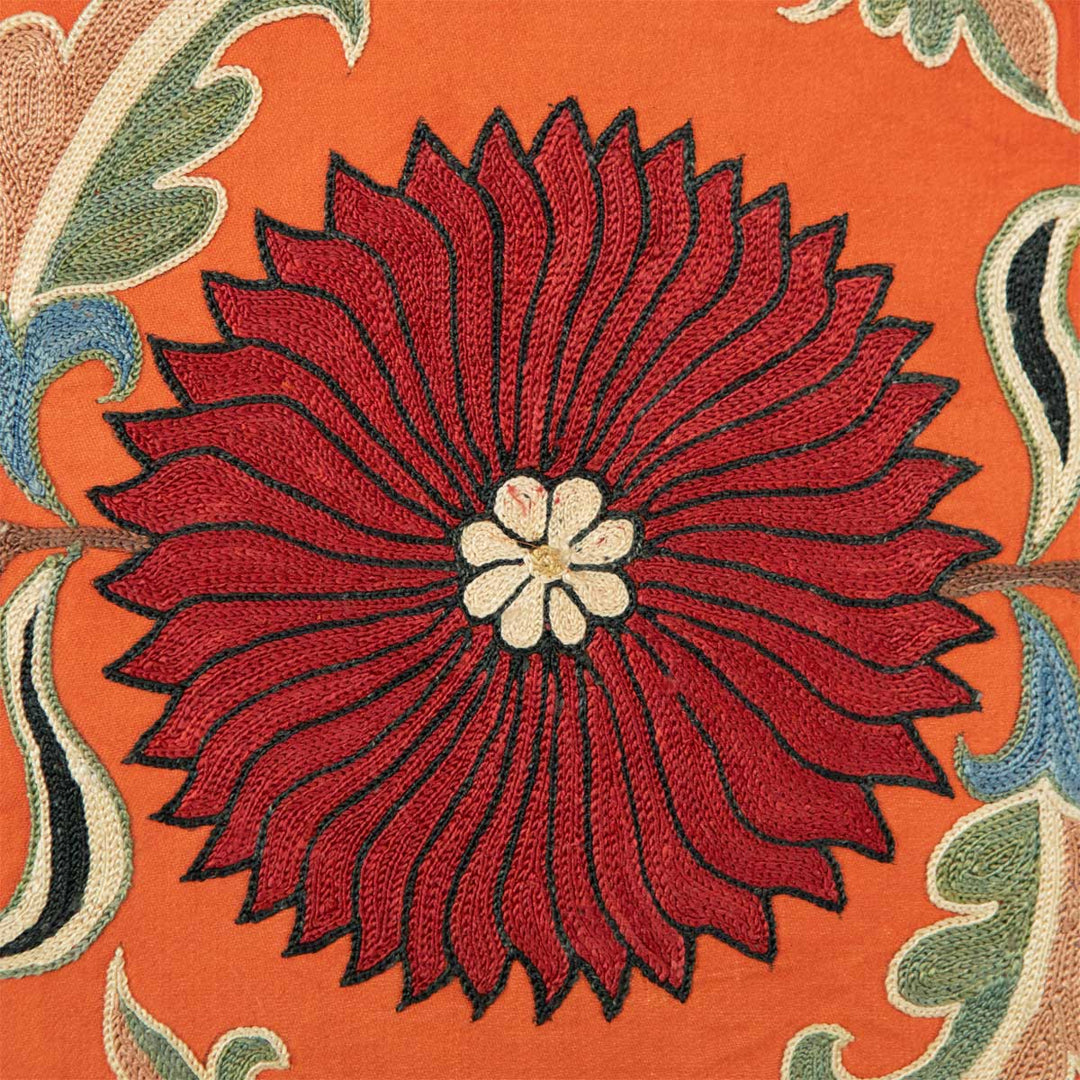 Close up view of Mekhann's orange silk floral artwork, showcasing a bright, hand embroidered, red silk flower with a white centre on the orange silk base fabric.