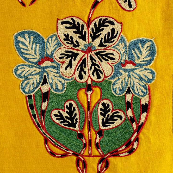 Detailed view of Mekhann's baroque yellow petite throw, showing the intricate detail of the baroque pattern embroidery in blue, cream, green, red and black, all set on the yellow silk base..