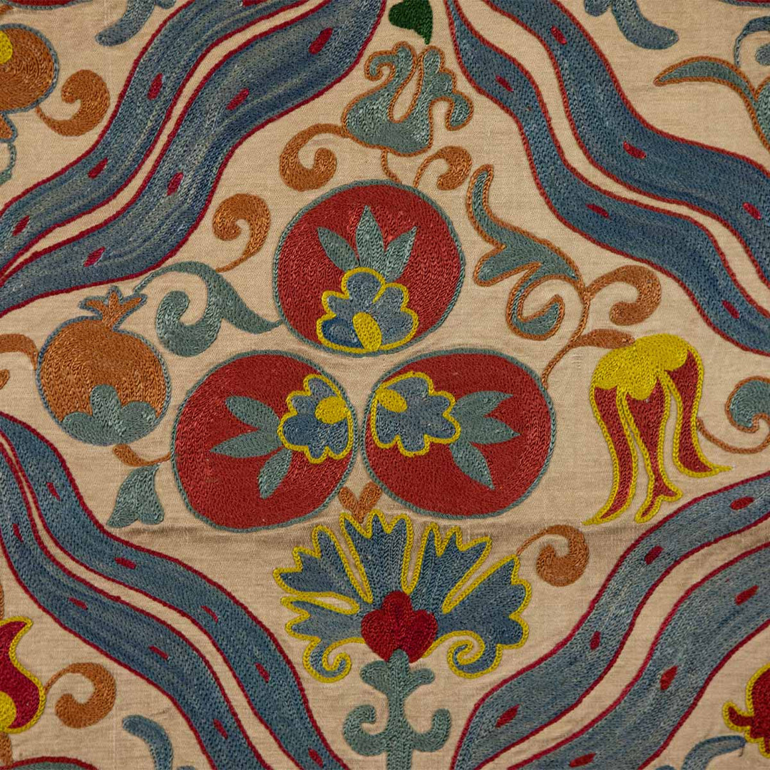 Close up view of Mekhann's multicoloured cintamani runner, displaying the hand embroidered cintamani motif in red and blue embroidered onto a cream silk background .