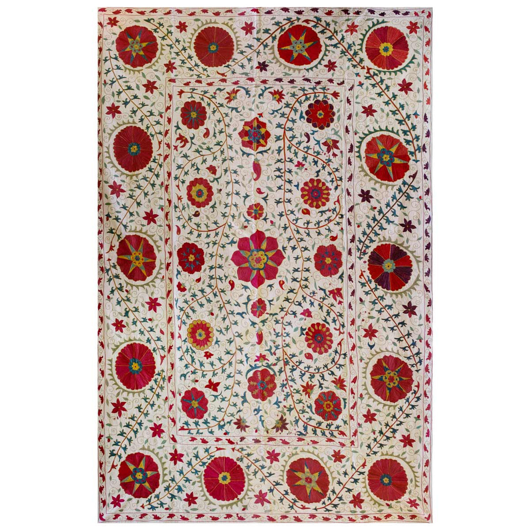 Front view of Mekhann's cream bukhara throw, with a full display of organic shapes in green and reds as the main embroidery colours. All of the botanical hand embroidered design elements have been set on a cream silk base.