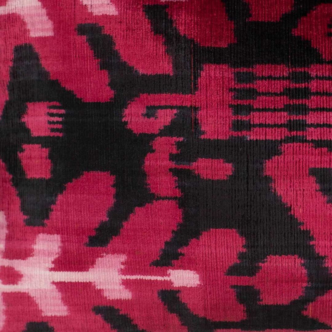 Close-up of handwoven silk velvet Ikat cushion in fuchsia and black, showcasing the intricate Sagitta pattern—crafted using traditional resist-dyeing techniques for a rich, blurred-edge effect.