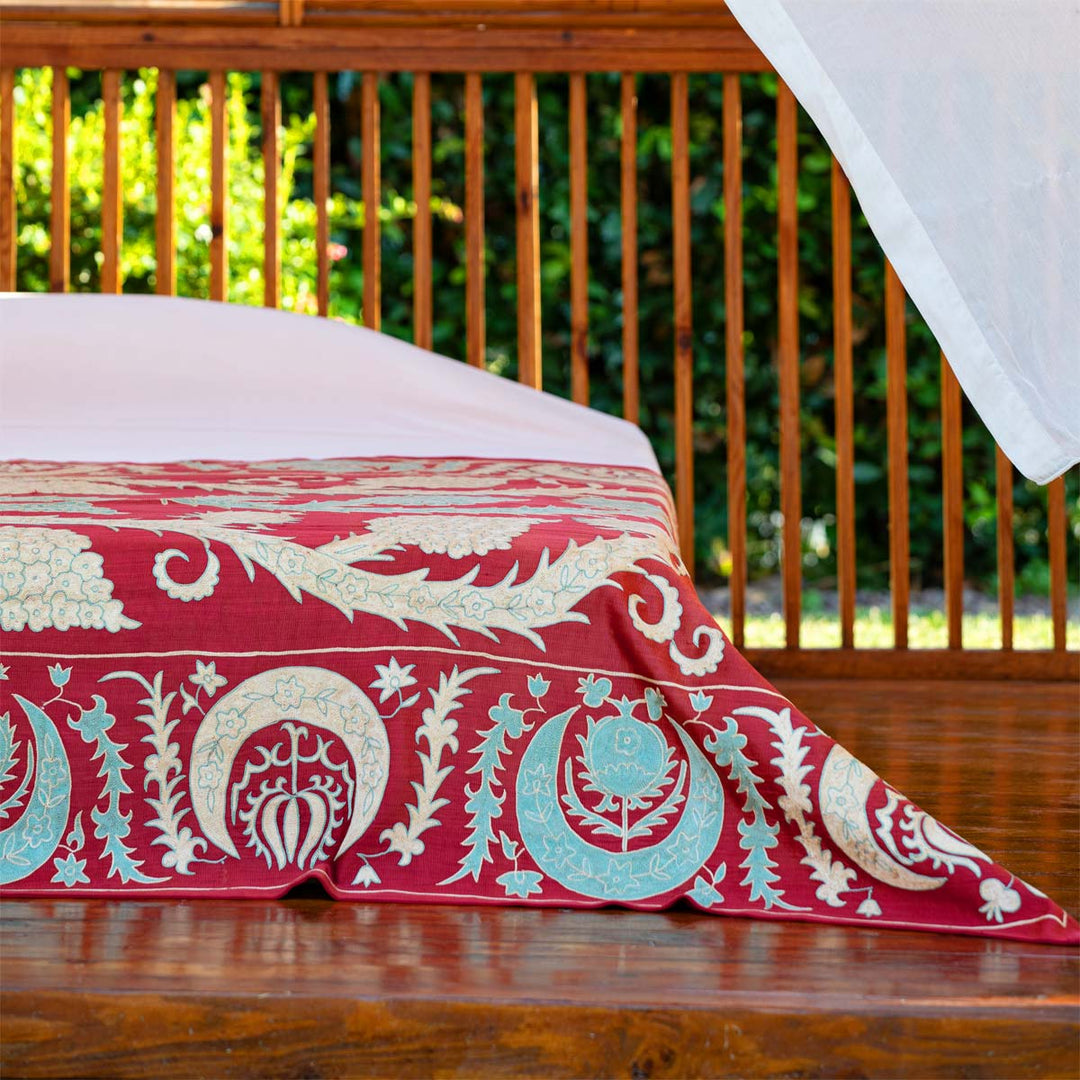 In use view of Mekhann's maroon grape vines throw, where the throw has been used as part of a bed spread and has been placed at the foot on the bed.