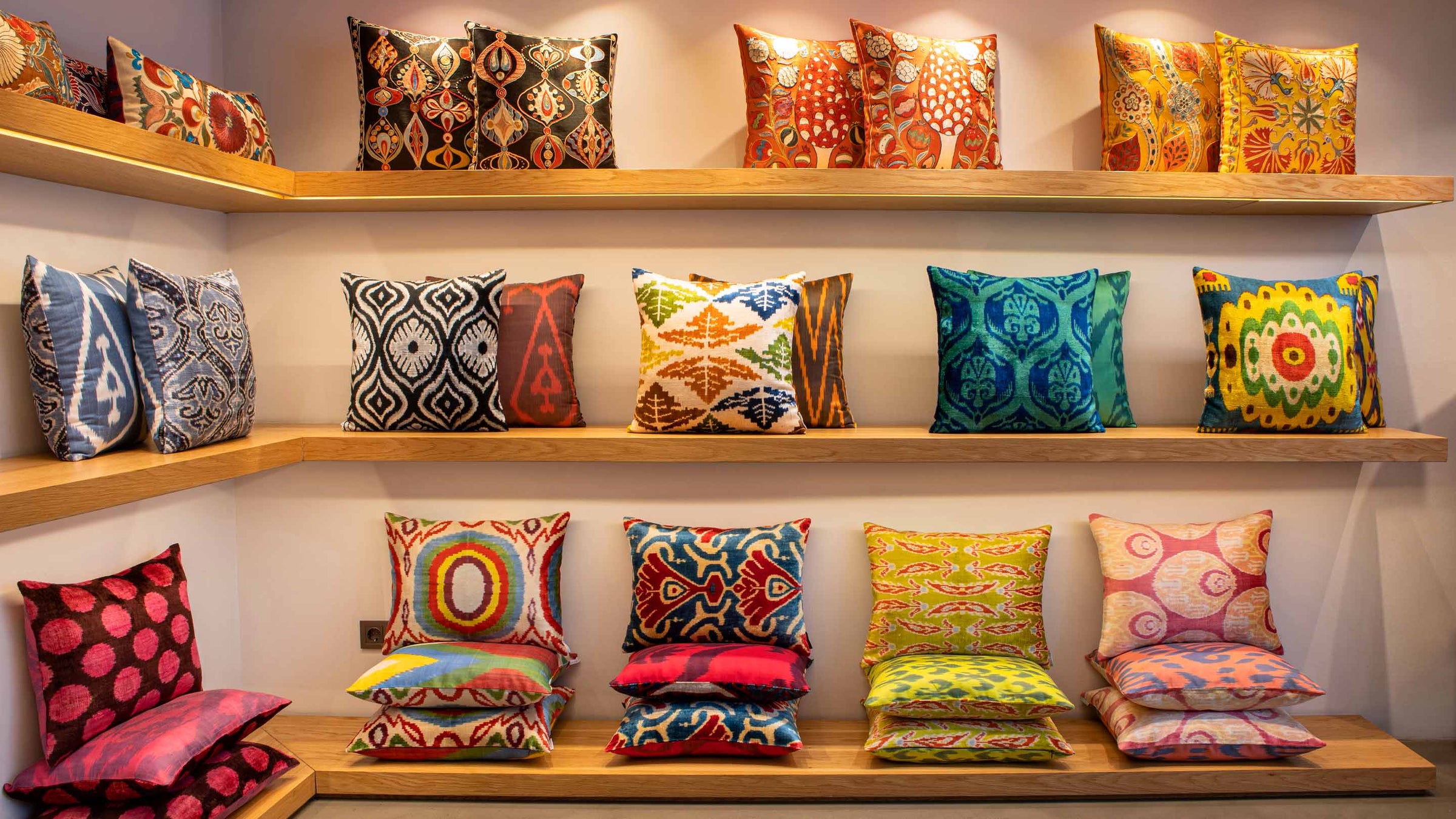 Collection of Mekhann embroidered silk and velvet designer cushions displayed on wooden shelves