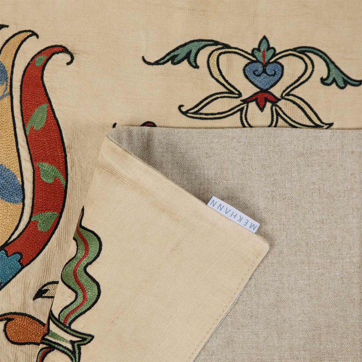 Corner fold of Mekhann's silk throw revealing the brand label, with traditional tulip embroidery pattern in the background, symbolising quality and heritage.