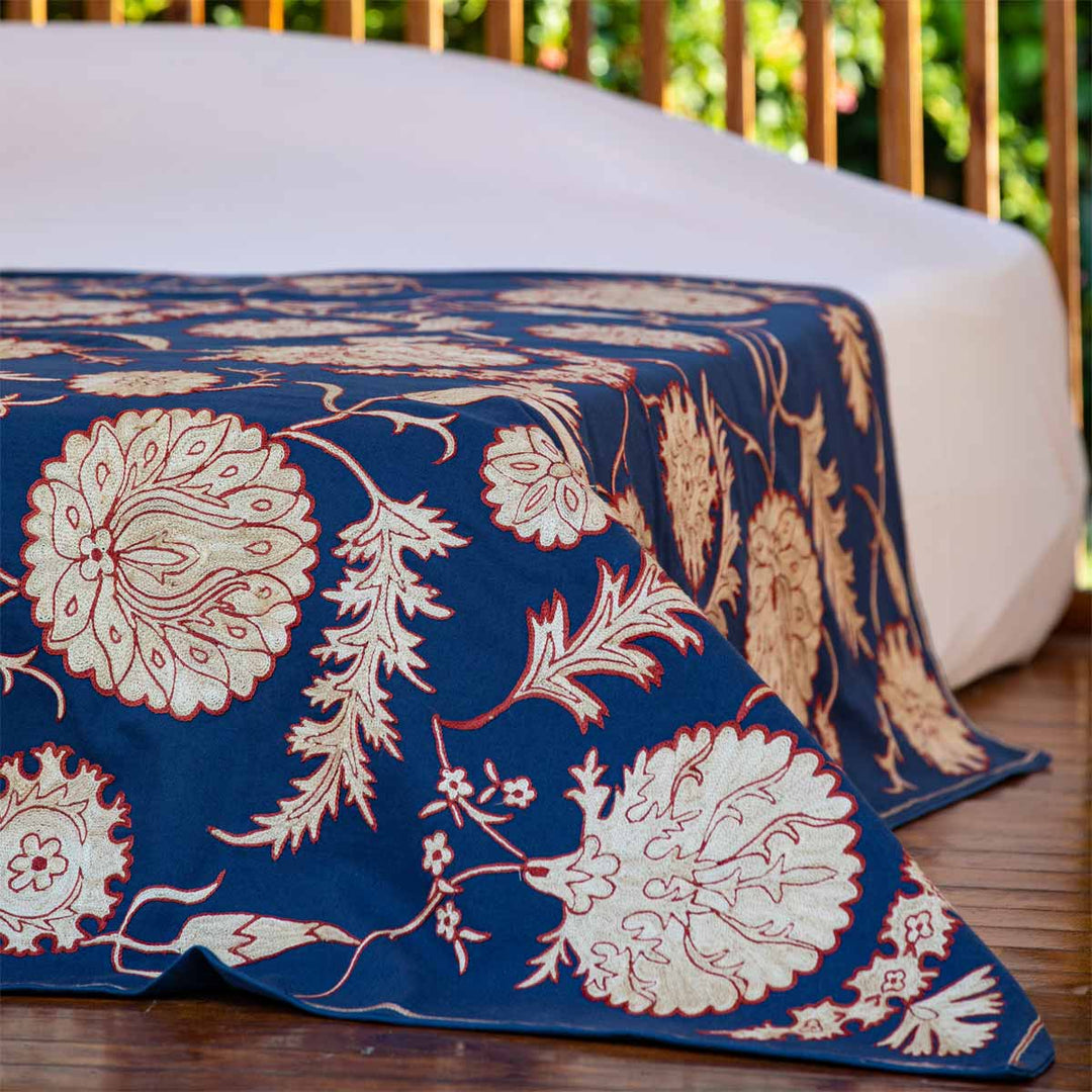 In use view of Mekhann's navy botanical throw, showing the navy botanical throw on the end of a bed with the cream botanical motifs in full view.