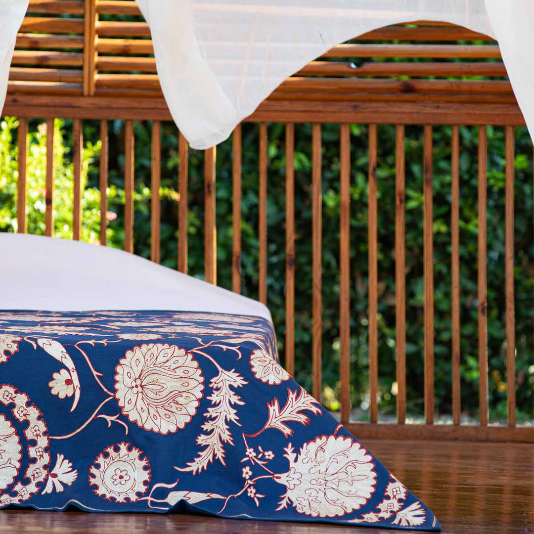 In use view of Mekhann's navy botanical throw, a wide display of the navy botanical throw on the end of a bed.