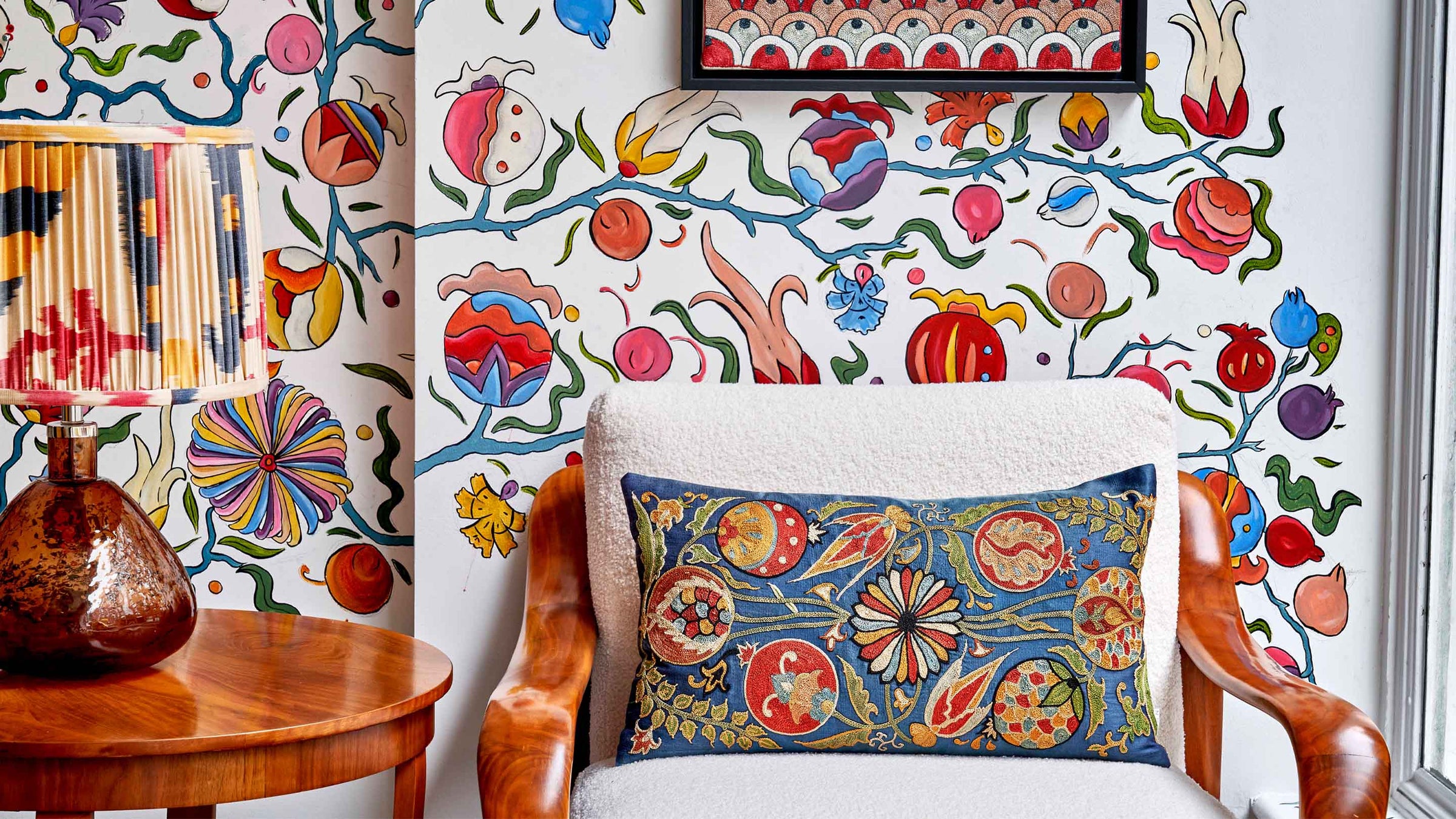 Navy rectangular suzani embroidered cushion by Mekhann displayed on an armchair with hand-painted floral mural in natural light