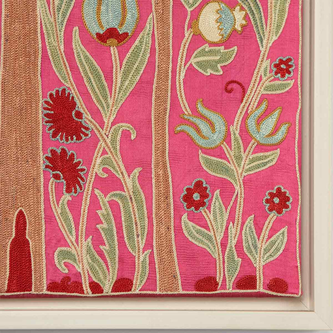 Corner view of Mekhann's pink silk cypress tree artwork, showing the contrast between the pink silk base, the organic green and beige embroidery, and the white frame.