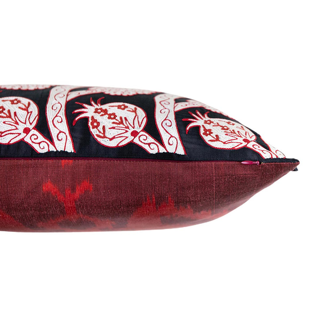 Side view of Mekhann's black grapes and pomegranates embroidered cushion, revealing how the black silk front face of the cushion meets the back, deep maroon ikat lining. 