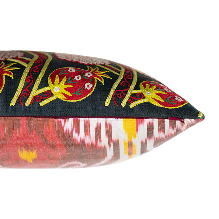 Side view of Mekhann's black grapes and pomegranates embroidered cushion, exposing how the front face of the cushion has been attached to the back lining which is a bright ikat fabric.