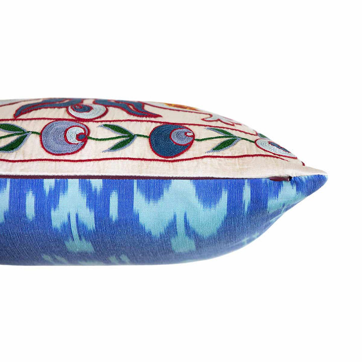 Side view of Mekhann's blue and multicoloured embroidered cushion, revealing the bright blue toned ikat back lining and where it meets the cream coloured silk from lining.