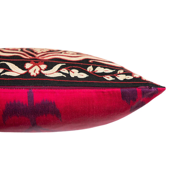 Side view of Mekhann's red and black carnations embroidered cushion, showing the point where the black silk front lining meets the back ikat lining in a bright pink.