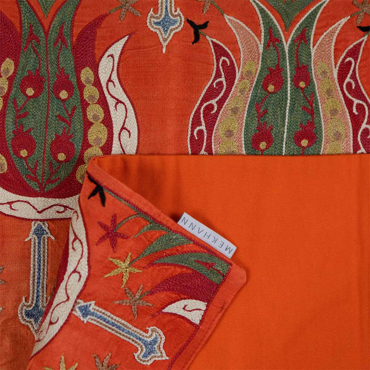 Folded view of Mekhann's clementine tulip petite throw, highlighting the elegant patterns and sumptuous fabric against the orange back lining with the Mekhann label.
