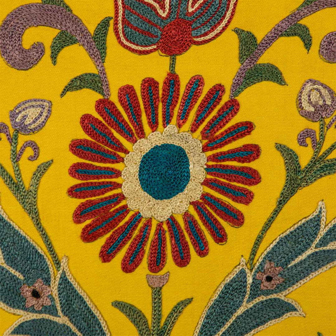 Up close view of Mekhann's yellow silk artwork with hand embroidered floral shapes. Revealing the main centre flower with blue and red embroidered petals embroidered onto a yellow silk base.