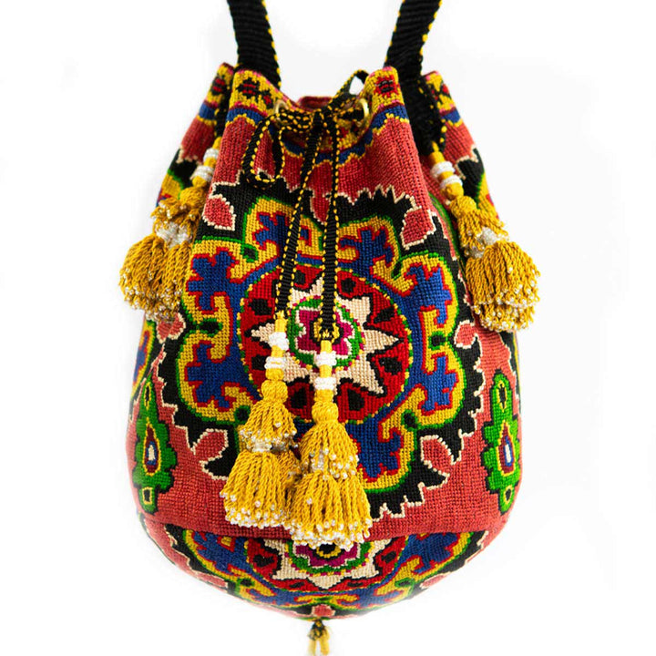 Front view of Mekhann's arabesque clementine embroidered bucket bag with a bold central pattern and gold and white tassel details.
