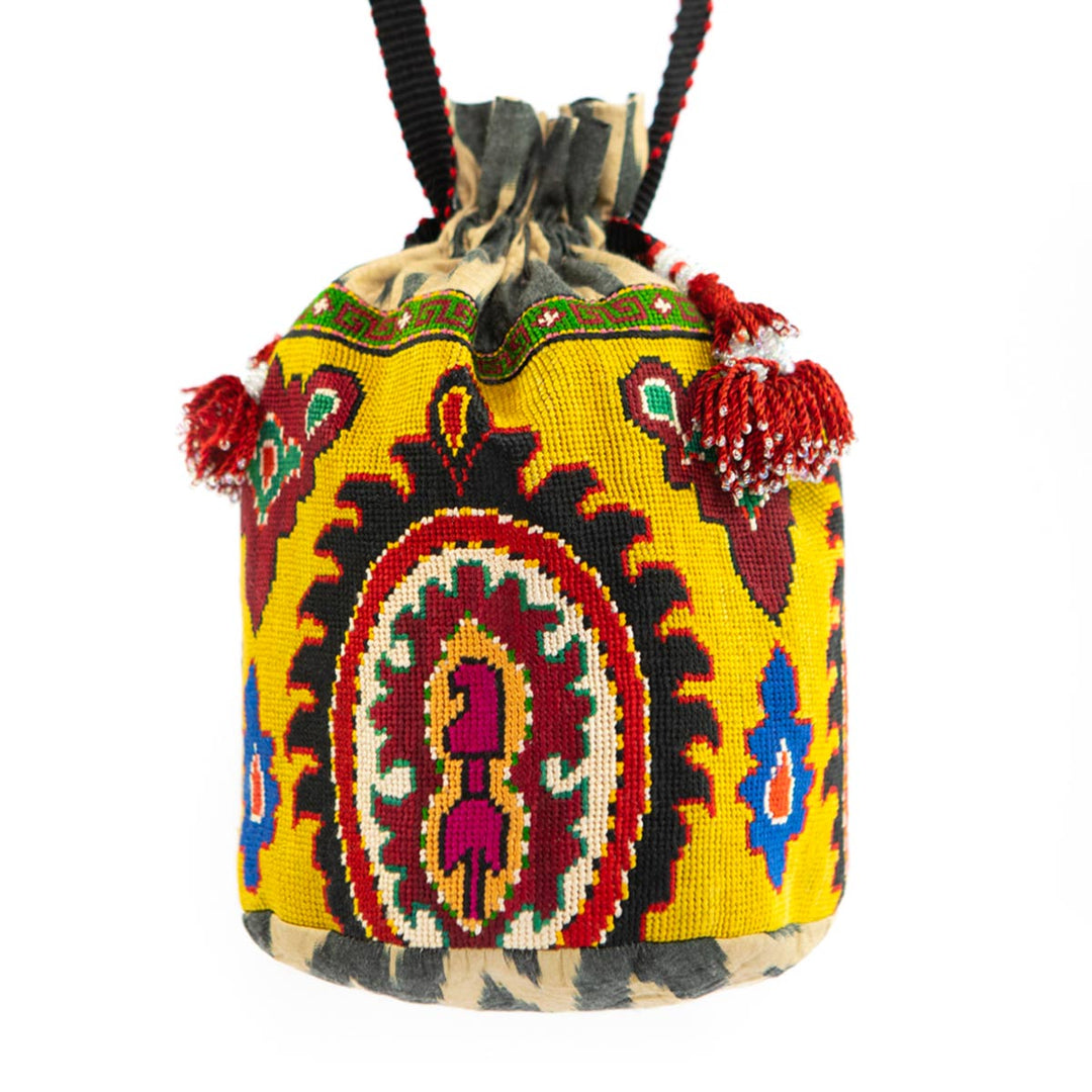 Front view of Mekhann's yellow arabesque embroidered bucket bag, showing the red tassels and the bold yellow surface colour. 