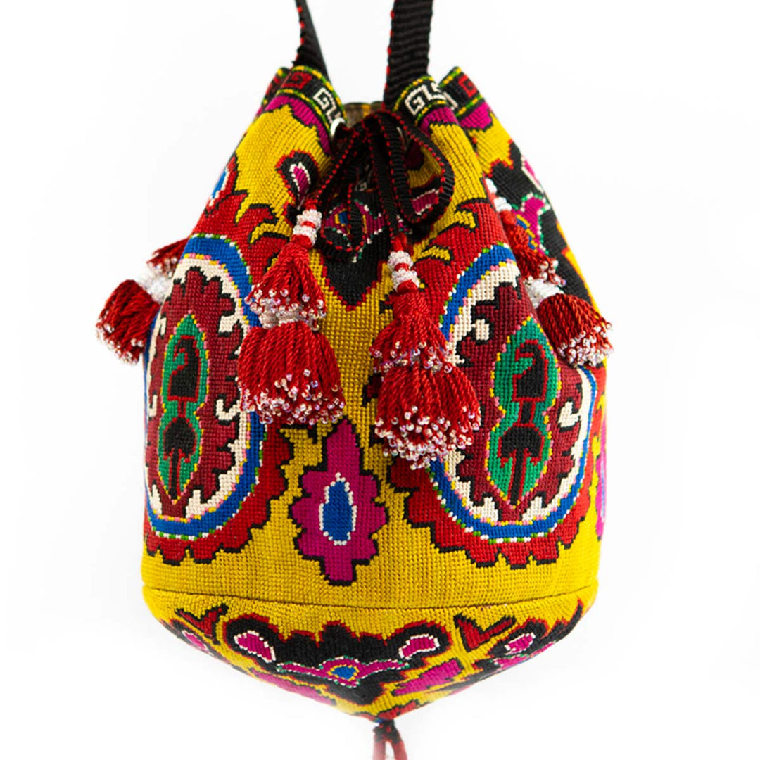 Front view of Mekhann's yellow arabesque embroidered bucket bag with a bold central patterns and red tassel details.