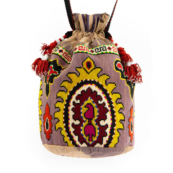 Front view of Mekhann's purple arabesque embroidered bucket bag, displaying the bold black strap with the red tassels on each side.