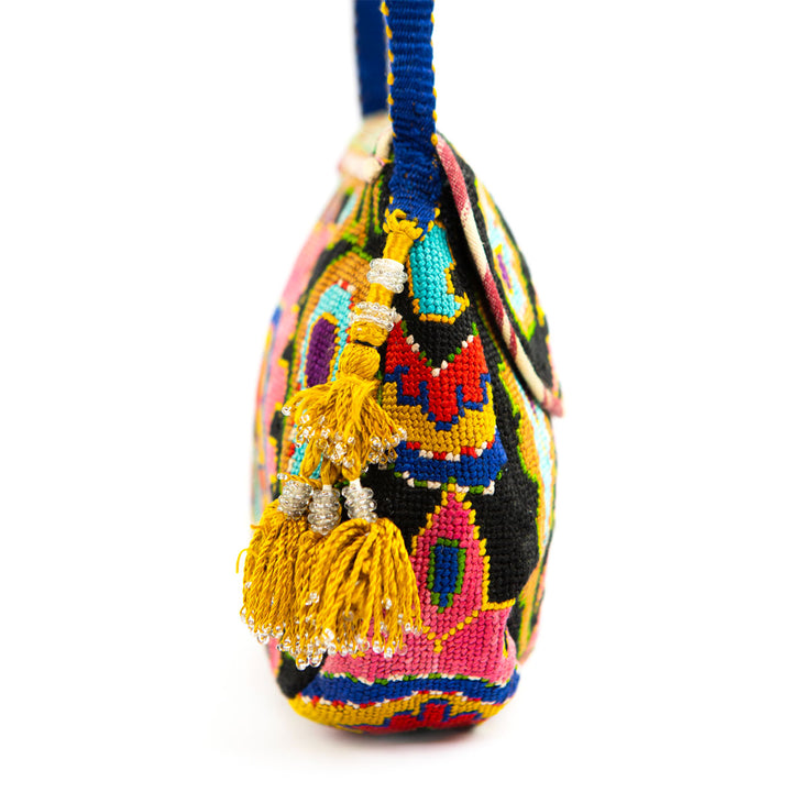 Side view of Mekhann's black and multicoloured arabesque embroidered cross-body bag, displaying it's bold blue strap with the bright yellow side tassels.