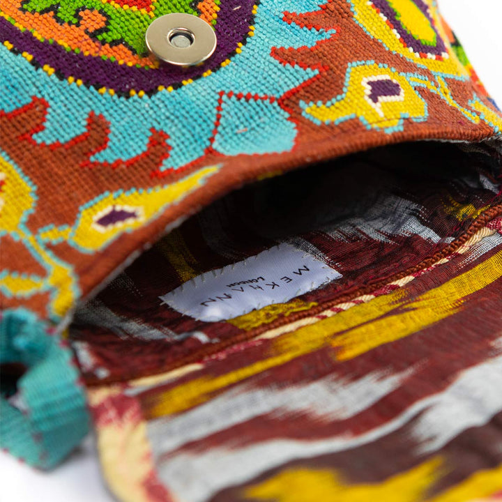 Inside view of Mekhann's blue and multicoloured arabesque embroidered cross-body bag, revealing a earth toned ikat lining.