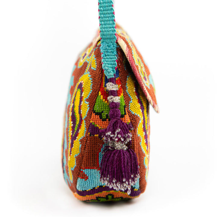 Side view of Mekhann's blue and multicoloured arabesque embroidered cross-body bag, showing off the bright blue strap and purple side tassel.