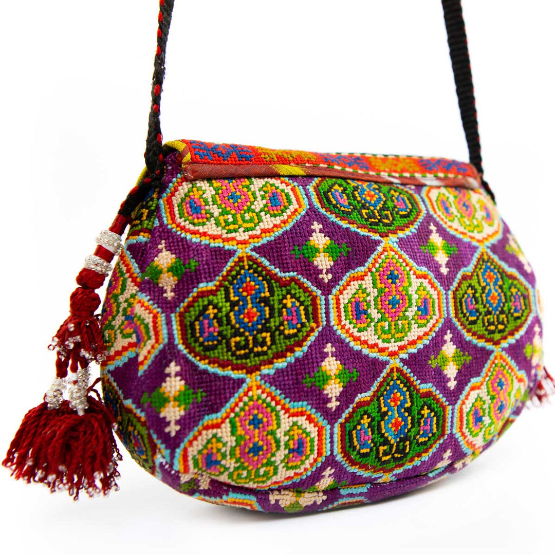 Back view of Mekhann's royal purple arabesque embroidered cross-body bag, showing the consistency in the patterns all over the bag, showing off the deep red tassels of the side of the bag.