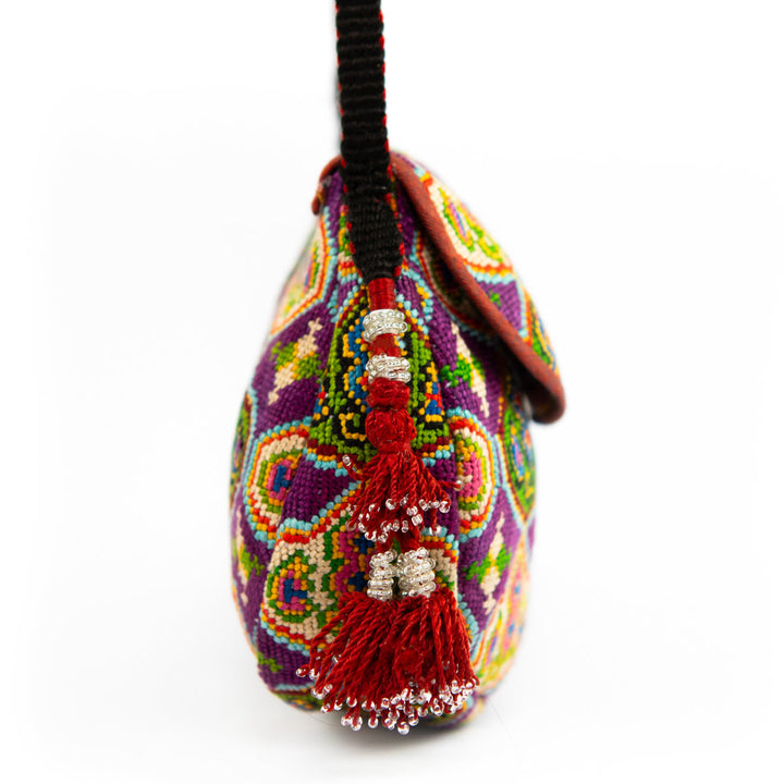Side view of Mekhann's royal purple arabesque embroidered cross-body bag, showcasing a the bold red tassel with the black strap.