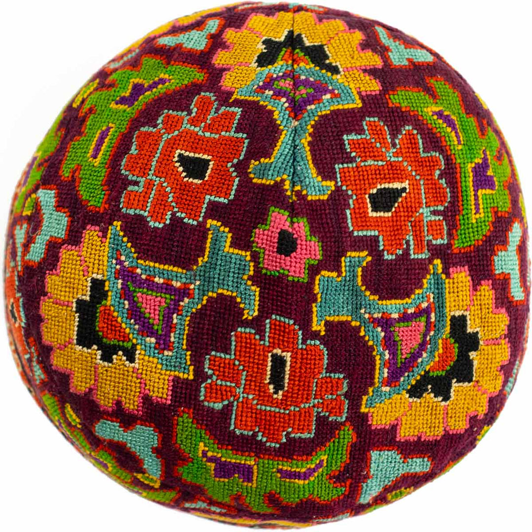 Top view of Mekhann's maroon arabesque skull cap, a bright display of hand embroidered patterns in yellow, red, blue and purple.