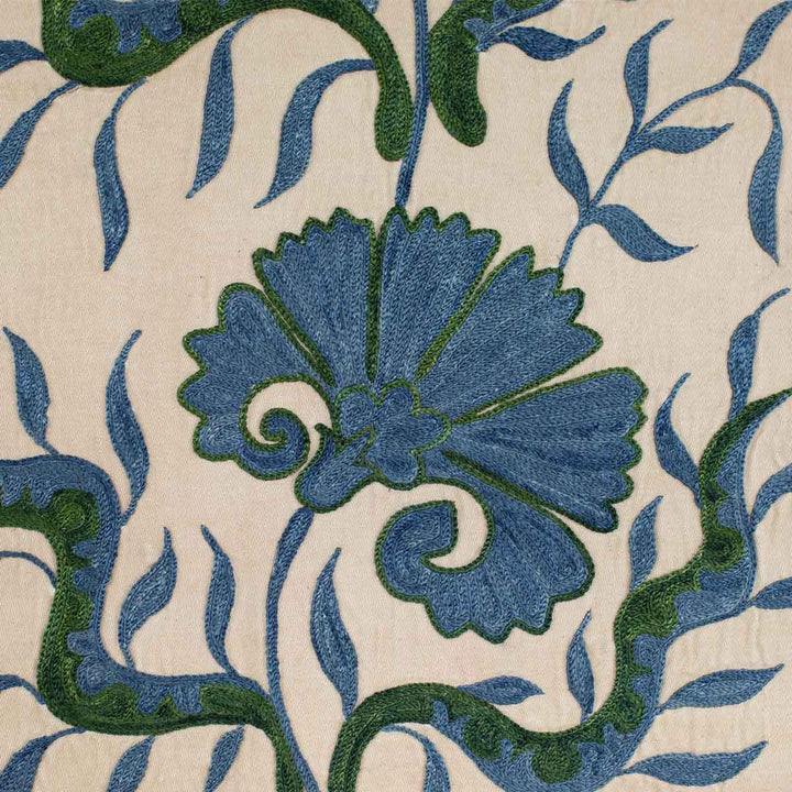 Close up view of Mekhann's cream ottoman vines runner, a close up of one of the hand embroidered motifs in blue and teal on a base of cream coloured silk.