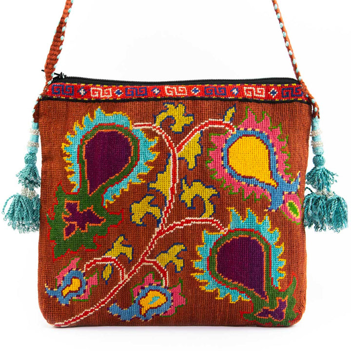 Front view of Mekhann's brown and multicoloured botanical embroidered cross-body, adorned with blue side tassels and a brown strap.