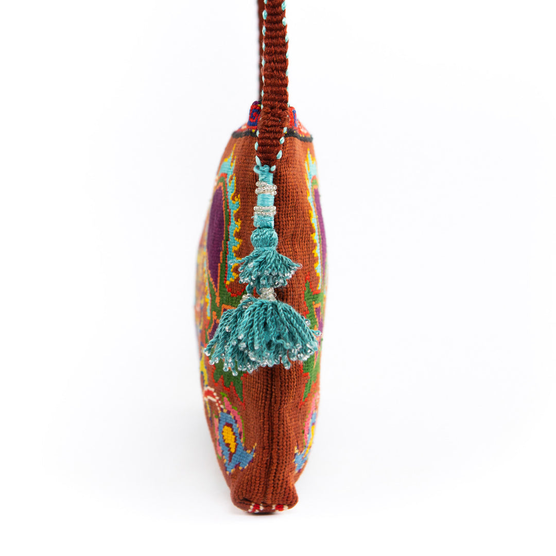 Side view of Mekhann's brown and multicoloured botanical embroidered cross-body, showcasing the bright blue tassels and the brown strap.